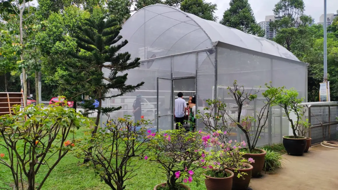 Arched greenhouse with mesh-covered walls and an entrance among landscaped planting