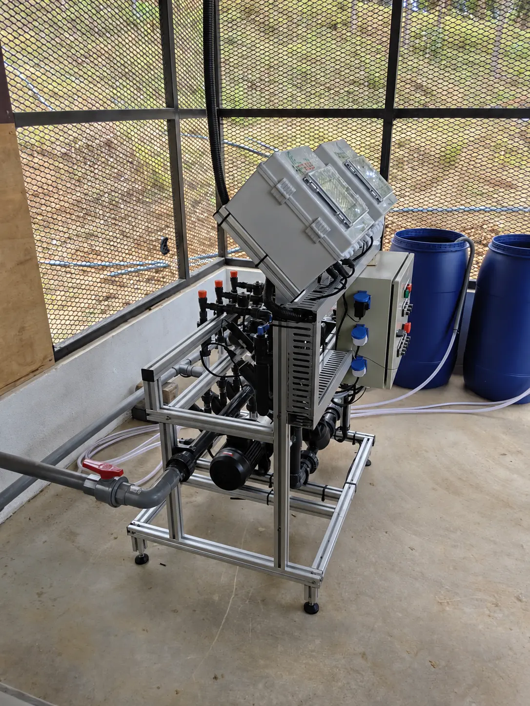 Fertigation dosing equipment, control enclosures, pipework and nutrient tanks inside a mesh enclosure